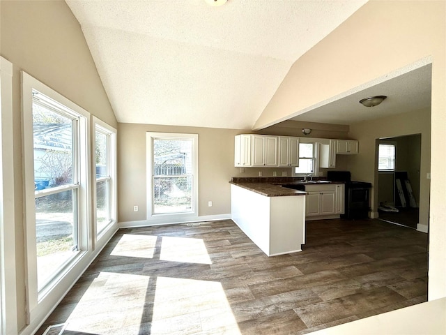 kitchen with dark countertops, vaulted ceiling, a peninsula, white cabinetry, and dark wood-type flooring