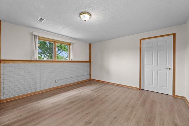 5099 Clover Ridge Rd, Panora, IA 50216 - unfurnished room featuring light wood-style floors, a textured ceiling, brick wall, baseboards, and visible vents