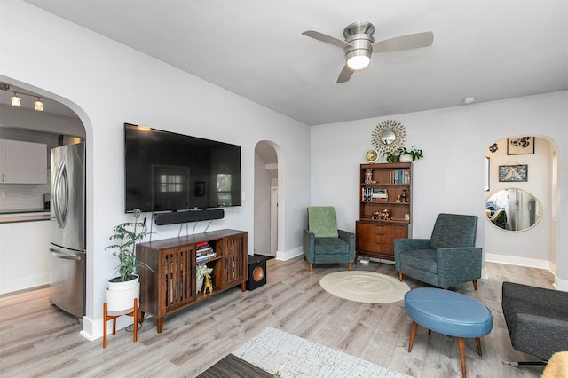 living area featuring arched walkways, ceiling fan, baseboards, and light wood finished floors