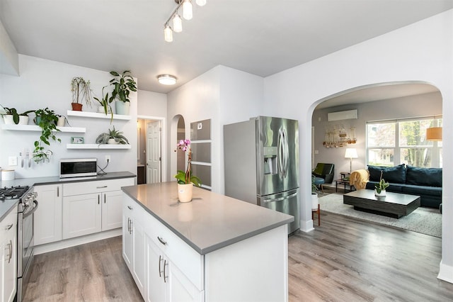 kitchen with arched walkways, appliances with stainless steel finishes, a wall unit AC, and light wood finished floors