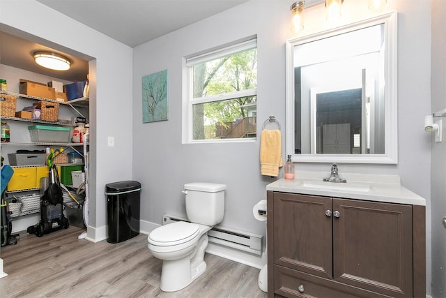 bathroom featuring vanity, wood finished floors, toilet, baseboards, and a baseboard heating unit