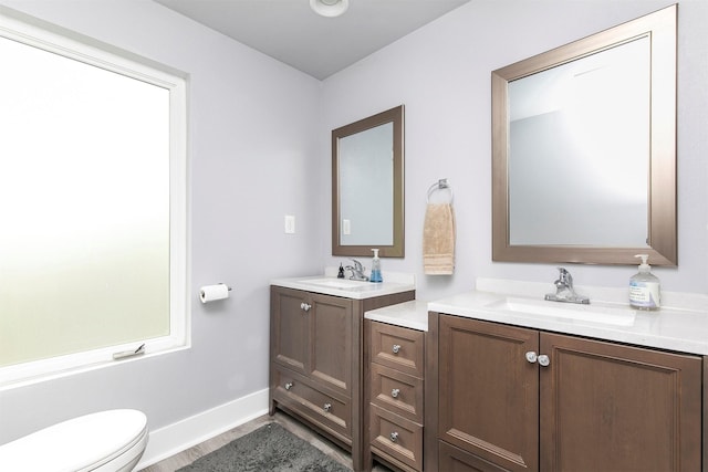 bathroom with wood finished floors, a sink, two vanities, and toilet