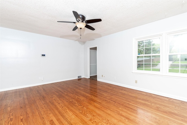 empty room with a ceiling fan, a textured ceiling, visible vents, and wood finished floors