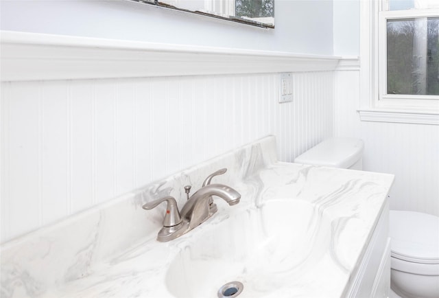 bathroom with vanity, wainscoting, a decorative wall, and toilet