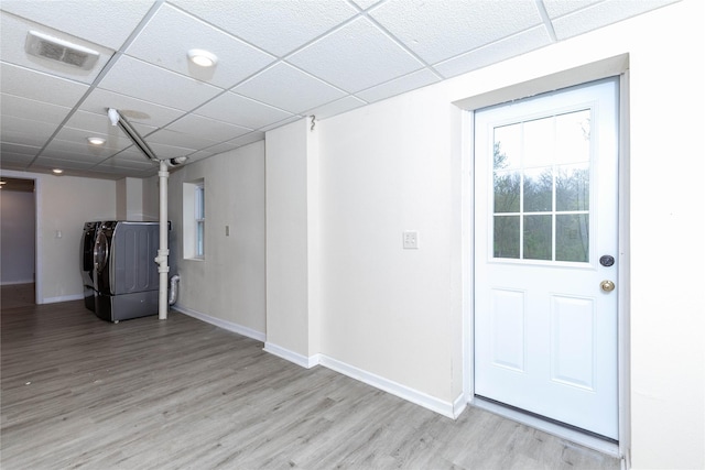 basement featuring visible vents, baseboards, a drop ceiling, washing machine and clothes dryer, and light wood-style flooring
