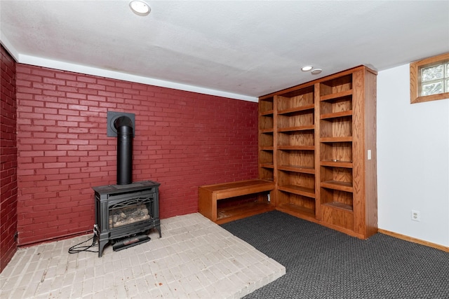 unfurnished living room featuring baseboards, a wood stove, recessed lighting, and brick wall