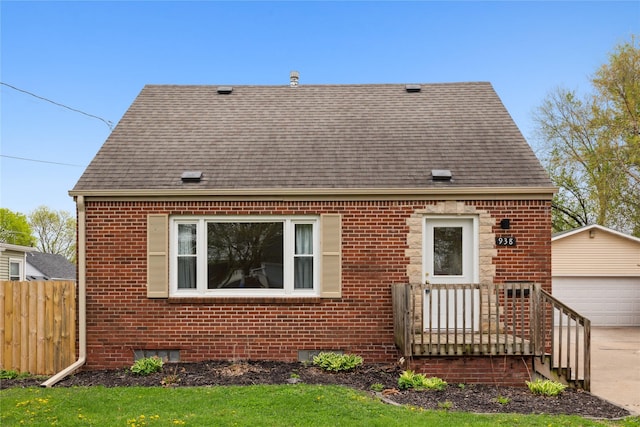 view of front of home featuring brick siding, fence, an outdoor structure, and roof with shingles