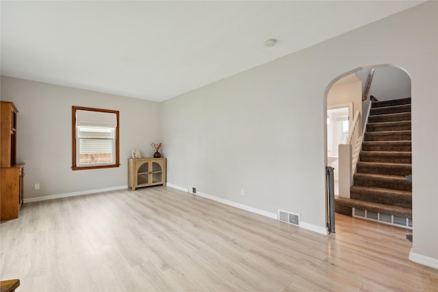 spare room with light wood-style floors, arched walkways, and visible vents