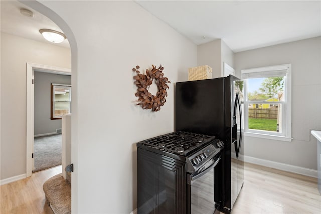 kitchen featuring light wood-style floors, arched walkways, baseboards, and black appliances