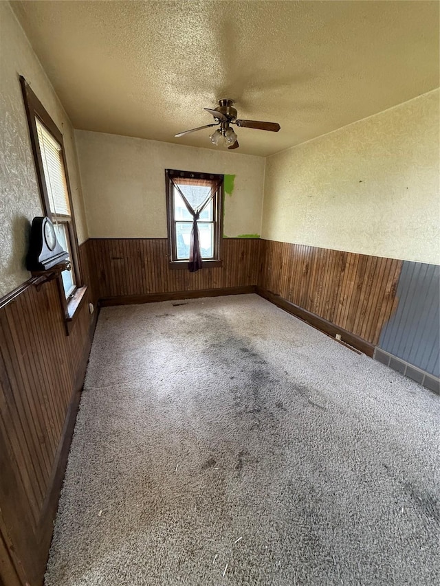 carpeted spare room featuring a textured wall, wooden walls, a textured ceiling, a wainscoted wall, and a ceiling fan