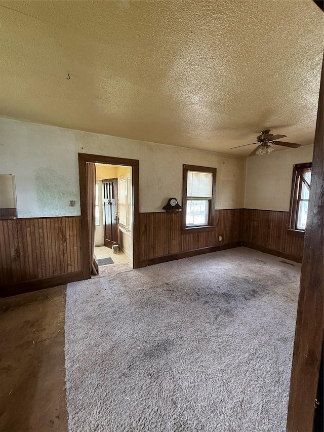 spare room with wooden walls, a wainscoted wall, ceiling fan, and a textured ceiling