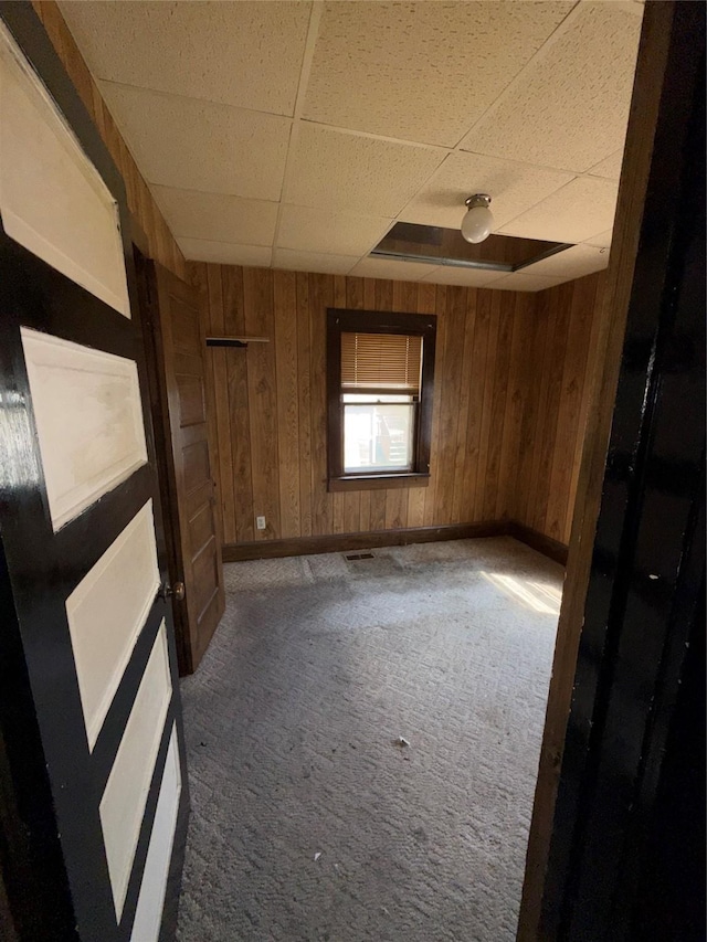 empty room featuring carpet floors, baseboards, wood walls, and a paneled ceiling