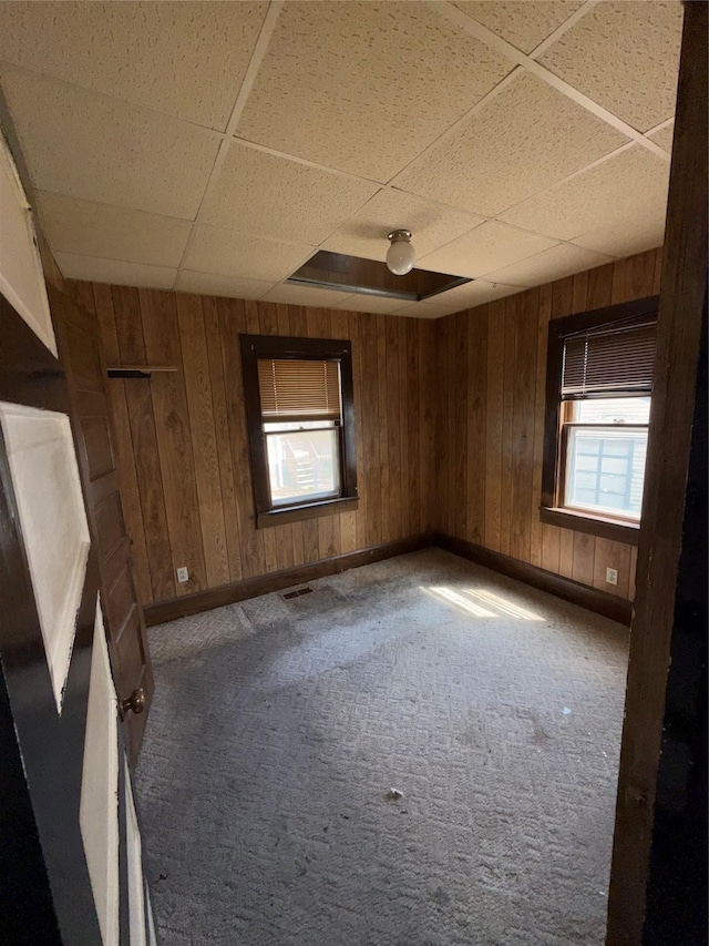 carpeted spare room with baseboards, wood walls, a drop ceiling, and visible vents