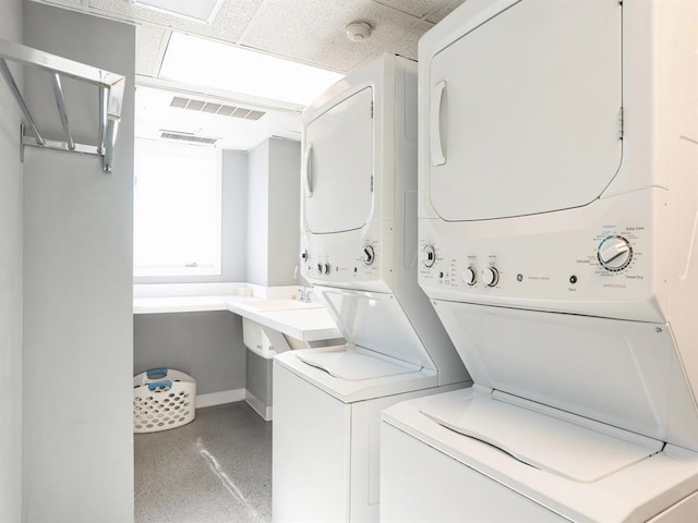 clothes washing area featuring baseboards, stacked washer and clothes dryer, and visible vents