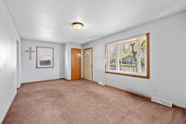 unfurnished room with carpet floors, visible vents, and plenty of natural light