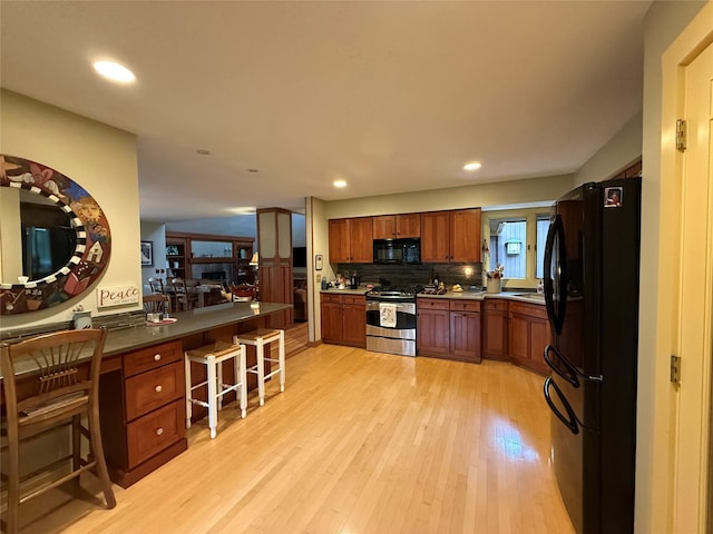 kitchen with a kitchen bar, brown cabinets, black appliances, recessed lighting, and light wood-style flooring