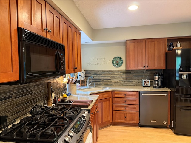 kitchen with brown cabinetry, light wood-type flooring, tasteful backsplash, a sink, and black appliances