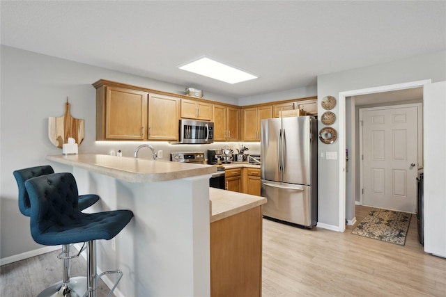 kitchen featuring appliances with stainless steel finishes, light countertops, a peninsula, light wood finished floors, and a breakfast bar