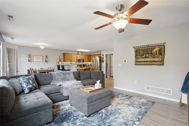 living room with light wood-style floors, baseboards, ceiling fan, and visible vents