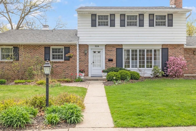 view of front of house featuring a chimney, brick siding, and a front yard