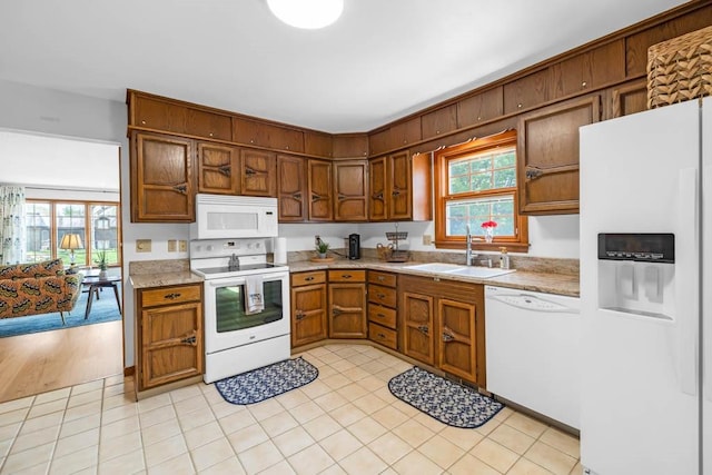 kitchen featuring brown cabinets, a sink, white appliances, light countertops, and plenty of natural light