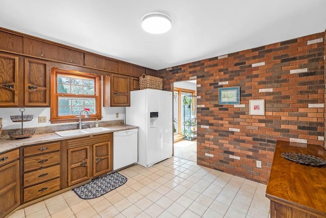 kitchen featuring white appliances, brick wall, brown cabinetry, and a sink