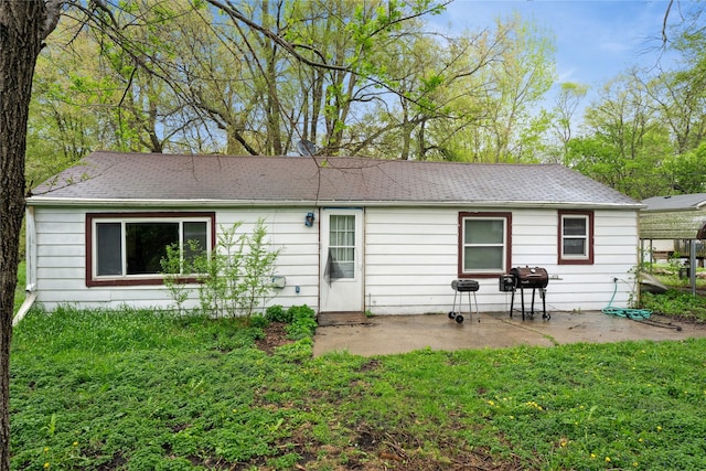 back of property featuring a lawn, a patio area, and roof with shingles