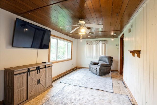 living area with wood ceiling, ceiling fan, baseboards, and wood walls