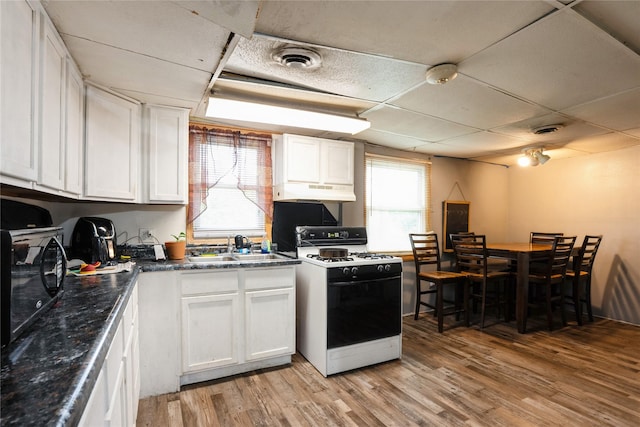 kitchen featuring dark countertops, light wood finished floors, white range with gas cooktop, and white cabinetry