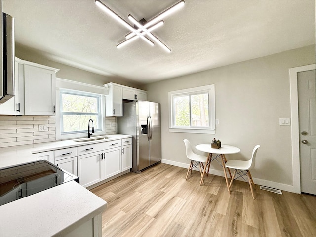 4825 SW 9th St, Des Moines, IA 50315 - kitchen featuring a sink, stainless steel fridge with ice dispenser, a textured ceiling, light countertops, and tasteful backsplash
