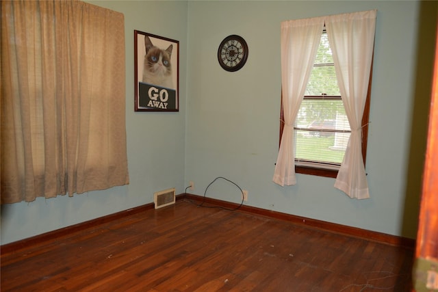 empty room featuring dark wood-style flooring, a healthy amount of sunlight, and visible vents
