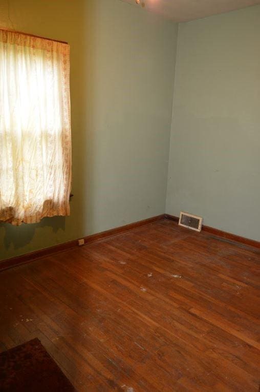 unfurnished room with baseboards, wood-type flooring, and visible vents