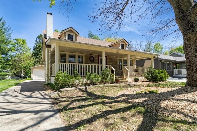 view of front of property with covered porch, a garage, a chimney, and an outbuilding
