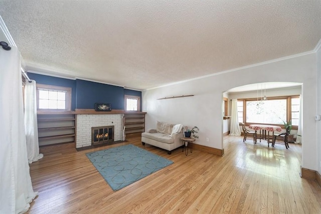 living room with wood finished floors, a healthy amount of sunlight, a textured ceiling, arched walkways, and ornamental molding