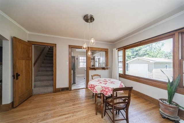 dining area with light wood finished floors, baseboards, ornamental molding, and stairs