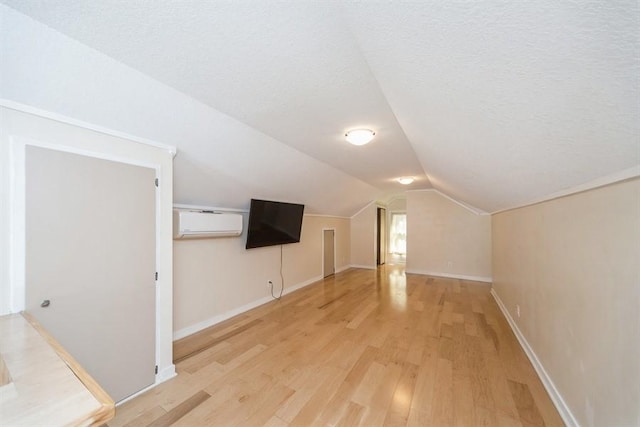 additional living space featuring vaulted ceiling, light wood finished floors, a wall mounted AC, and baseboards