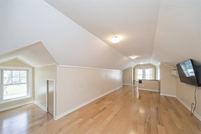 additional living space featuring light wood-style floors, vaulted ceiling, baseboards, and a textured ceiling