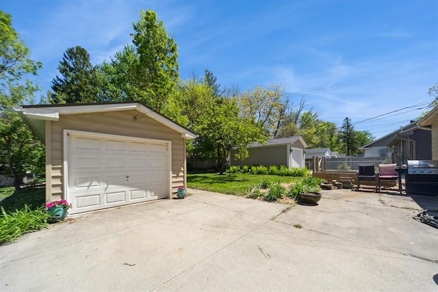 detached garage featuring concrete driveway and fence