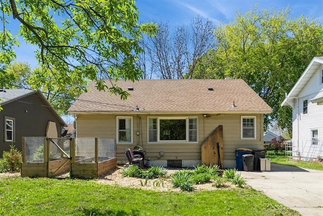 rear view of house featuring roof with shingles, concrete driveway, and a lawn