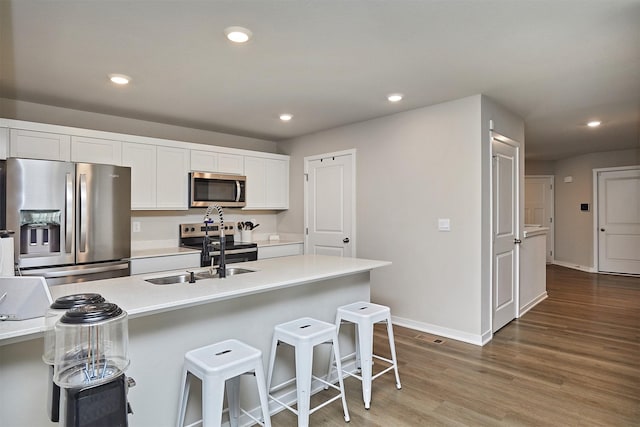 1150 NW Williamsburg Ln, Waukee, IA 50263 - kitchen featuring appliances with stainless steel finishes, white cabinets, a breakfast bar, light wood-type flooring, and baseboards