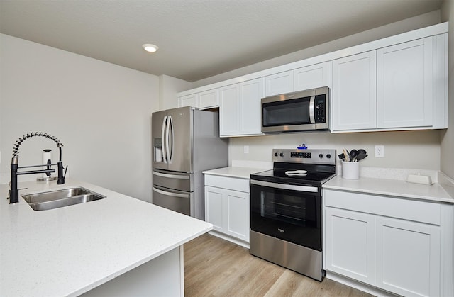 1150 NW Williamsburg Ln, Waukee, IA 50263 - kitchen with stainless steel appliances, a sink, light wood-style flooring, white cabinets, and recessed lighting