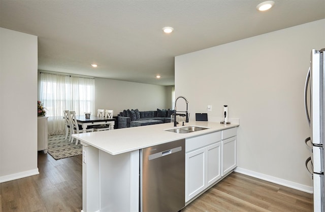 1150 NW Williamsburg Ln, Waukee, IA 50263 - kitchen with stainless steel appliances, a sink, a peninsula, light wood-type flooring, and white cabinetry