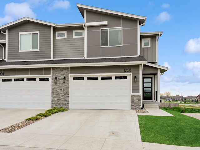 view of front of house featuring stone siding, an attached garage, driveway, and a front yard