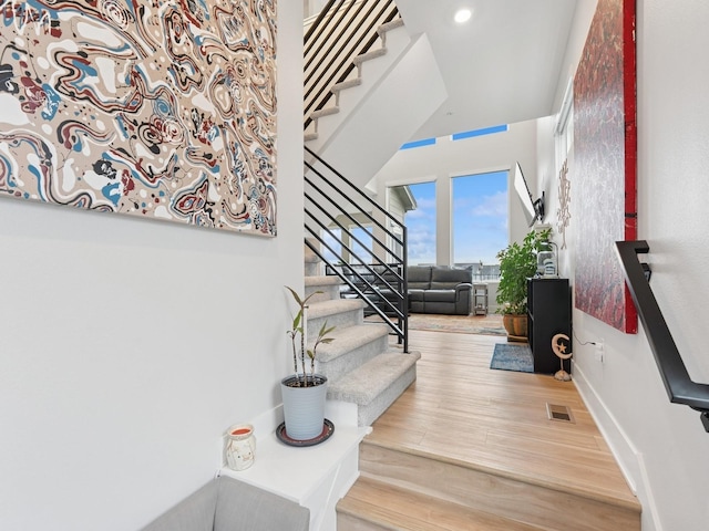 stairway featuring wood finished floors, a towering ceiling, visible vents, recessed lighting, and baseboards