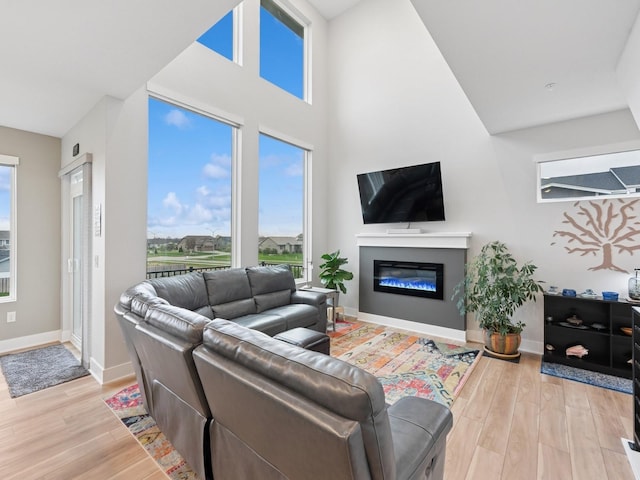 living area with light wood-style floors, baseboards, a towering ceiling, and a glass covered fireplace