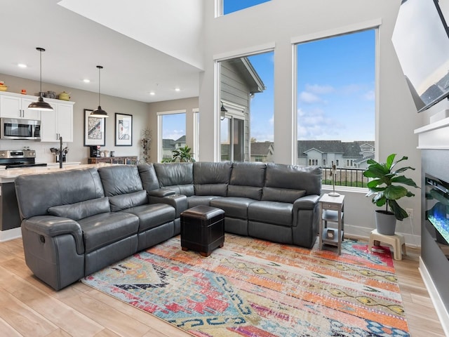 living area with recessed lighting, light wood-type flooring, baseboards, and a glass covered fireplace