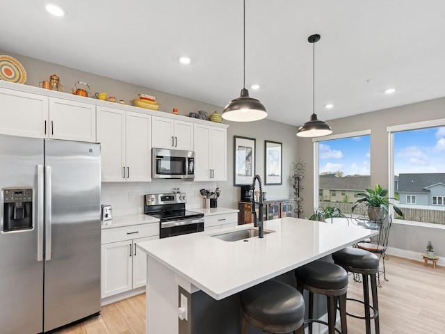 kitchen featuring light wood-style flooring, a sink, a kitchen island with sink, appliances with stainless steel finishes, and tasteful backsplash