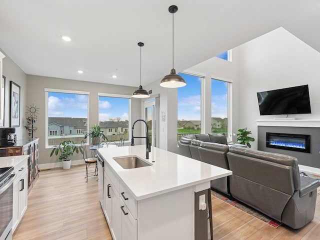kitchen with a sink, white cabinetry, open floor plan, and light wood-type flooring