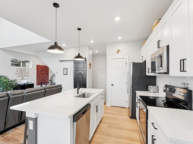 kitchen featuring a sink, a barn door, a center island with sink, open floor plan, and appliances with stainless steel finishes