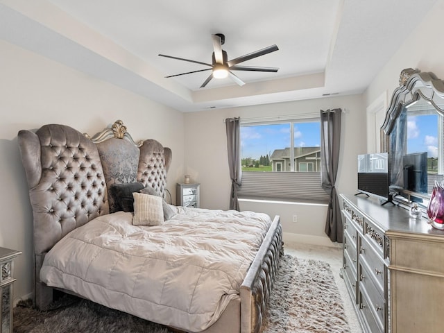 bedroom featuring a tray ceiling, baseboards, a ceiling fan, and light colored carpet